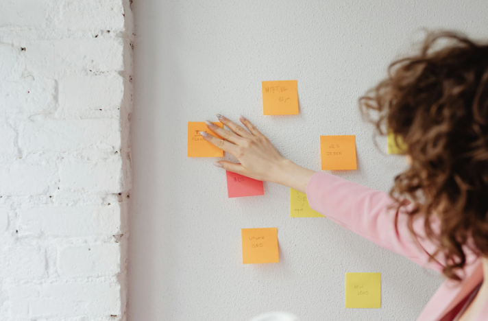 Woman in a pink blazer organizing sticky notes on a wall, mapping out the top skills for a real estate agent in 2025.