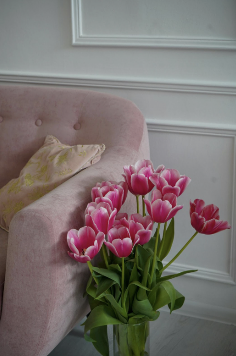 Pink tulips in a glass vase placed beside a blush velvet chair, styled as part of open house staging.